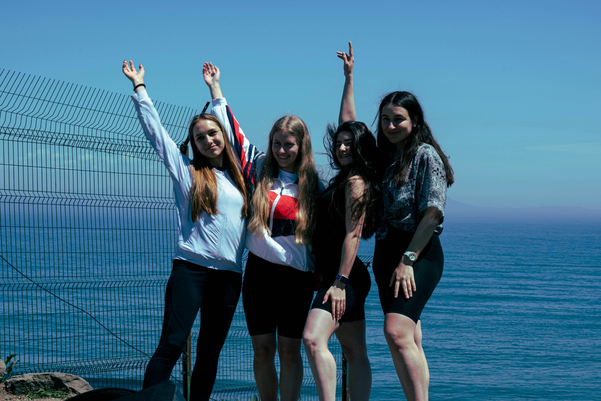 Grupo de amigas a celebrar com braços ao alto frente ao mar durante uma caça ao tesouro urbana